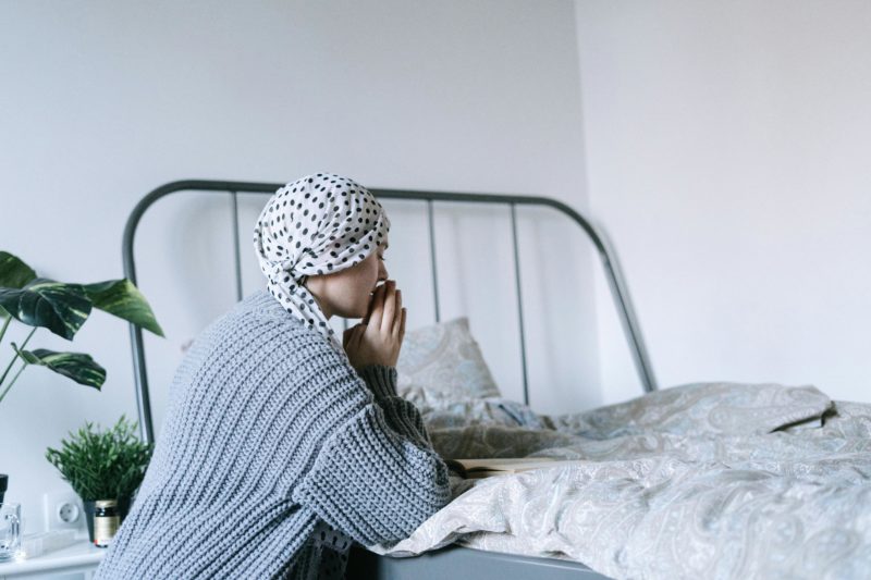 A woman in a headscarf sits by her bed reflecting and gathering courage.