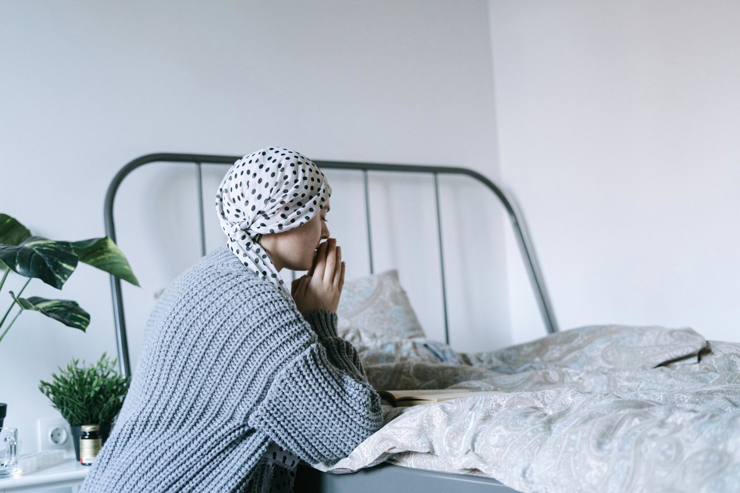 A woman in a headscarf sits by her bed reflecting and gathering courage.